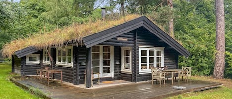 Una cabaña de troncos con techo de paja, terraza de madera y un letrero que dice 'Krathuset'.