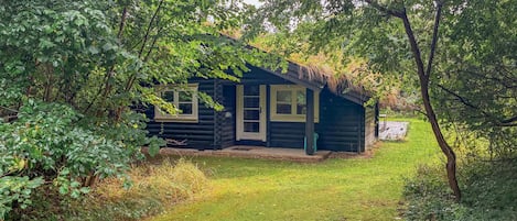 A log cabin with a porch, surrounded by dense foliage.