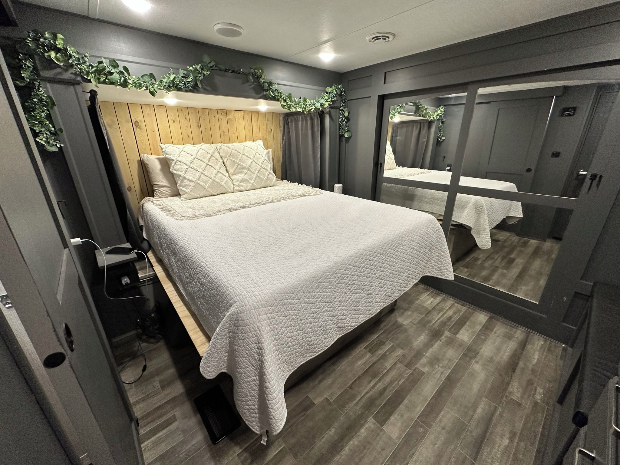 A compact bedroom with a bed, a bedside table, a mirror, and a wardrobe.