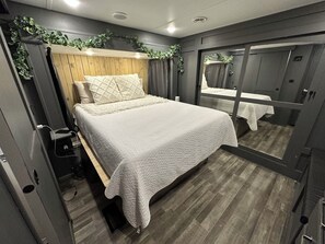 A compact bedroom with a bed, a bedside table, a mirror, and a wardrobe. - The Avalanche at River Rocks Landing (Gadsden)