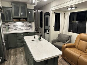A compact RV kitchen with a central island, built-in cabinets, and a gray couch. - The Avalanche at River Rocks Landing (Gadsden)
