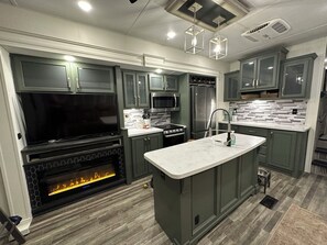 A modern kitchen with a built-in fireplace, stainless steel appliances, and a central island. - The Avalanche at River Rocks Landing (Gadsden)