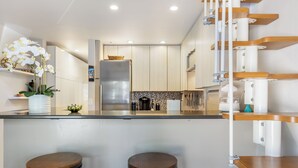 A modern kitchen with a central island, two bar stools, and a staircase with wooden steps. - Beautiful 1 Bedroom Vail Condo 700 meters from Cascade Lift (Vail)
