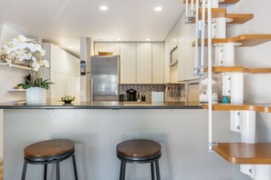 A modern kitchen with a central island, two bar stools, and a staircase with wooden steps. - Beautiful 1 Bedroom Vail Condo 700 meters from Cascade Lift (Vail)