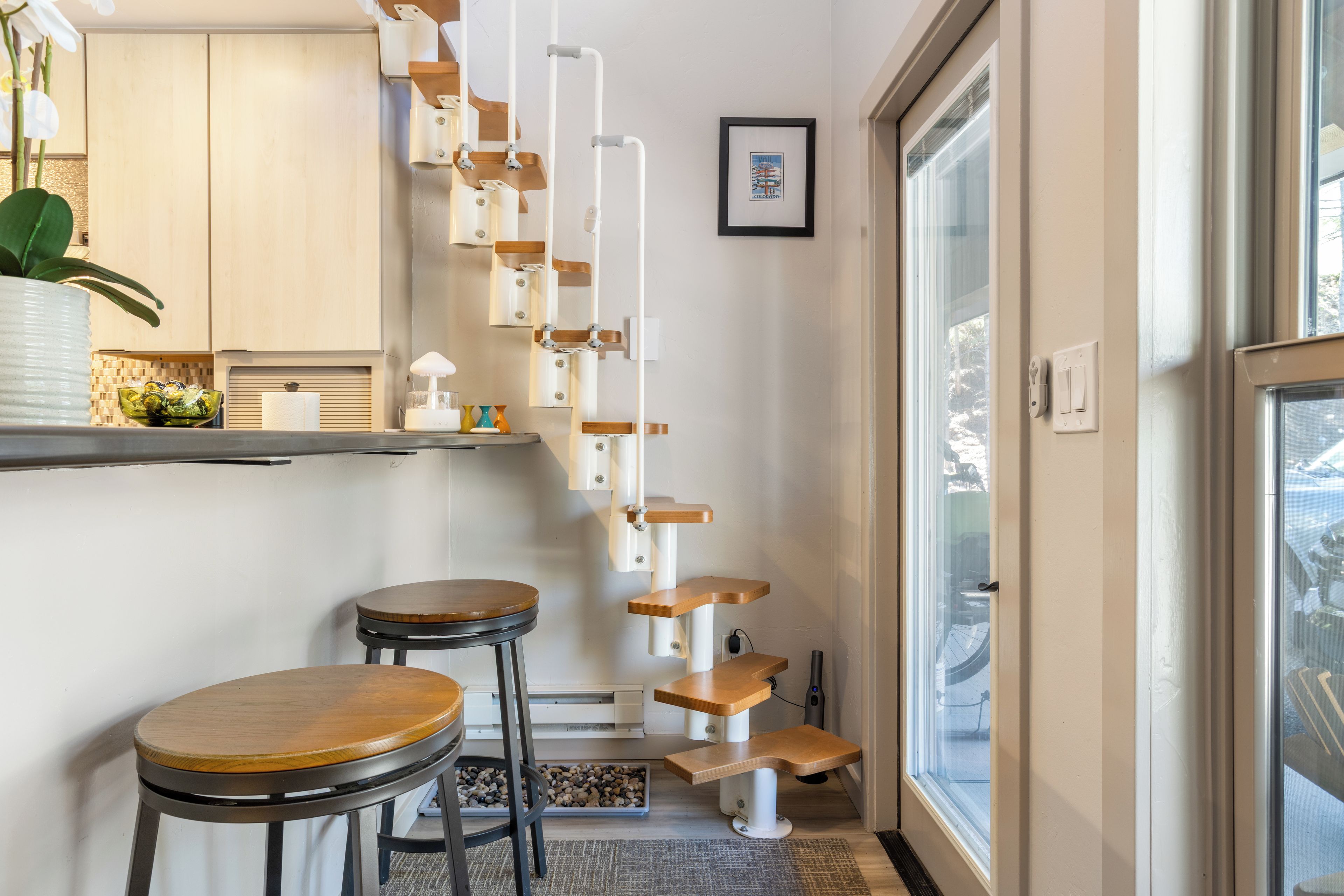 Une cuisine moderne avec un plan de travail blanc, un tabouret de bar en bois et un arbre à chat suspendu.