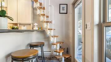 A modern kitchen with a white countertop, a wooden bar stool, and a hanging cat tree.
