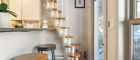Une cuisine moderne avec un plan de travail blanc, un tabouret de bar en bois et un arbre à chat suspendu.