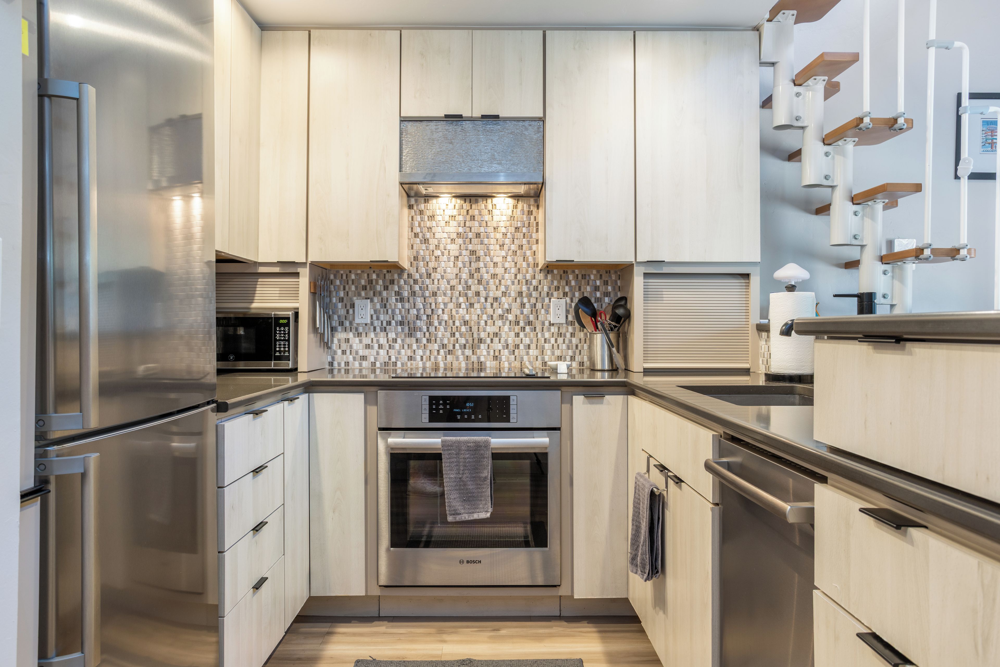 A modern kitchen with stainless steel appliances, wooden cabinets, and a patterned backsplash.