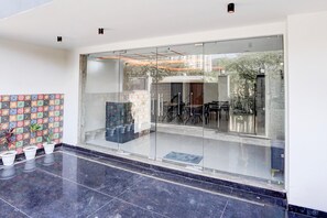 A modern interior with a glass entrance, a tiled wall with a floral pattern, and potted plants. - Deluxe Townhouse Sector 143b (Noida)