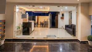 A modern interior with a glass entrance, a dining area with chairs and a table, and a sofa. - Deluxe Townhouse Sector 143b (Noida)