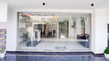 A modern entrance with a glass door leading to a dining area, a seating arrangement, and a view of the outside.