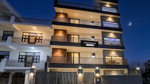 A multi-story building with balconies, a sign indicating 'Townhouse & Company Services,' and a gated entrance. - Deluxe Townhouse Sector 143b (Noida)