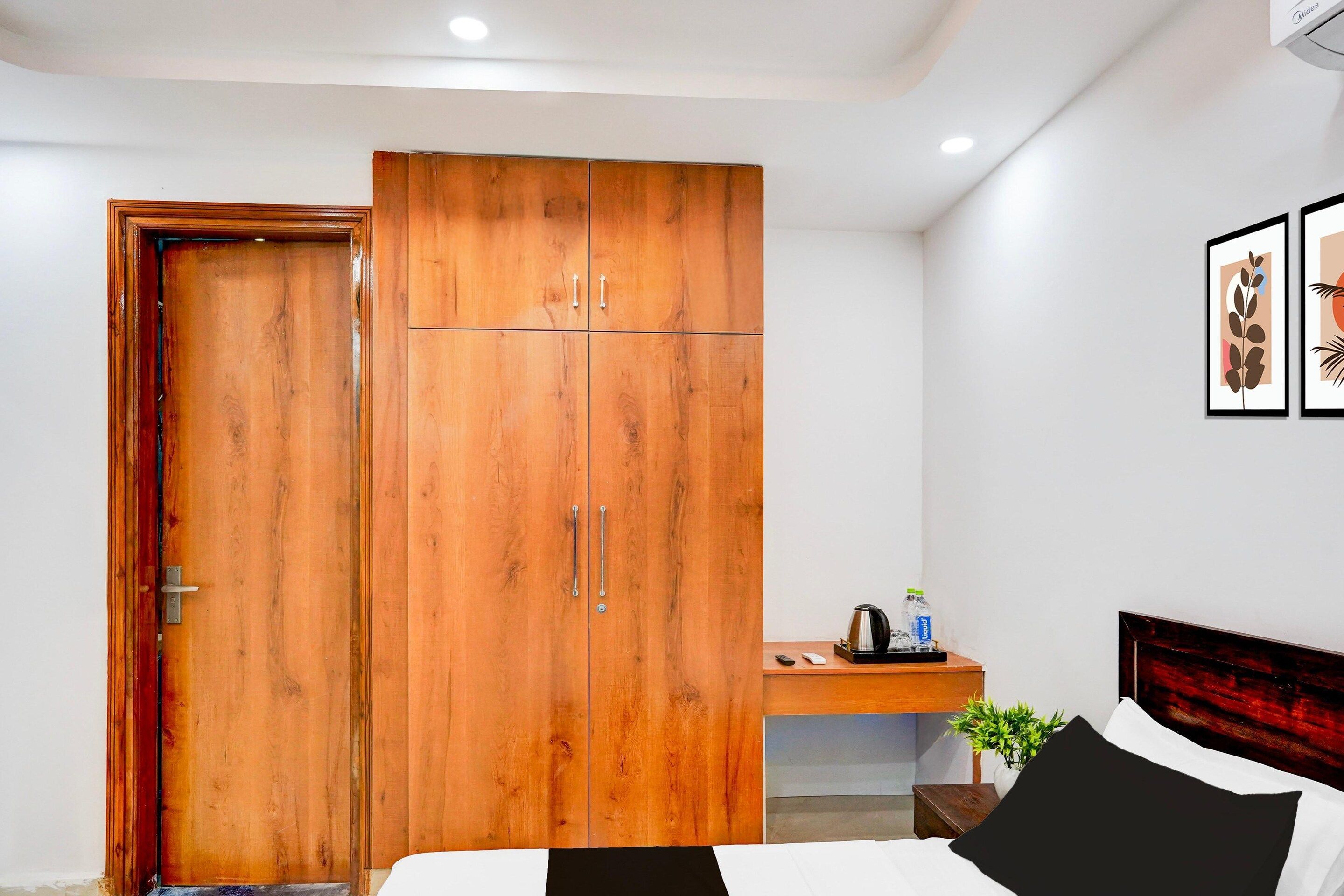 A bedroom with a wooden wardrobe, a bed, a bedside table with a kettle, and a framed picture on the wall.