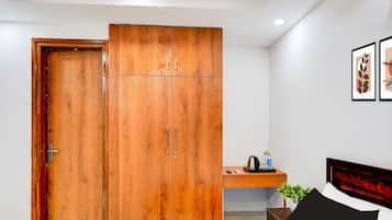 A bedroom with a wooden wardrobe, a bed, a bedside table with a kettle, and a framed picture on the wall.