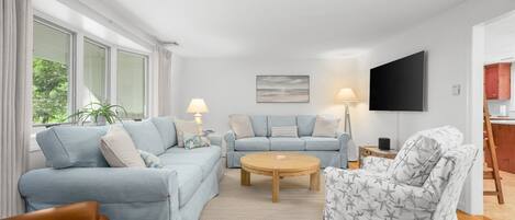 Una sala de estar con sofá, sillón, mesa de centro y televisor de pantalla plana.