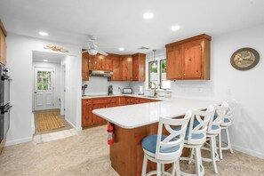 A kitchen with wooden cabinets, a white countertop, and a bar area with white chairs. - Close to Mayflower Beach with deck, yard, and A/C. (Dennis)