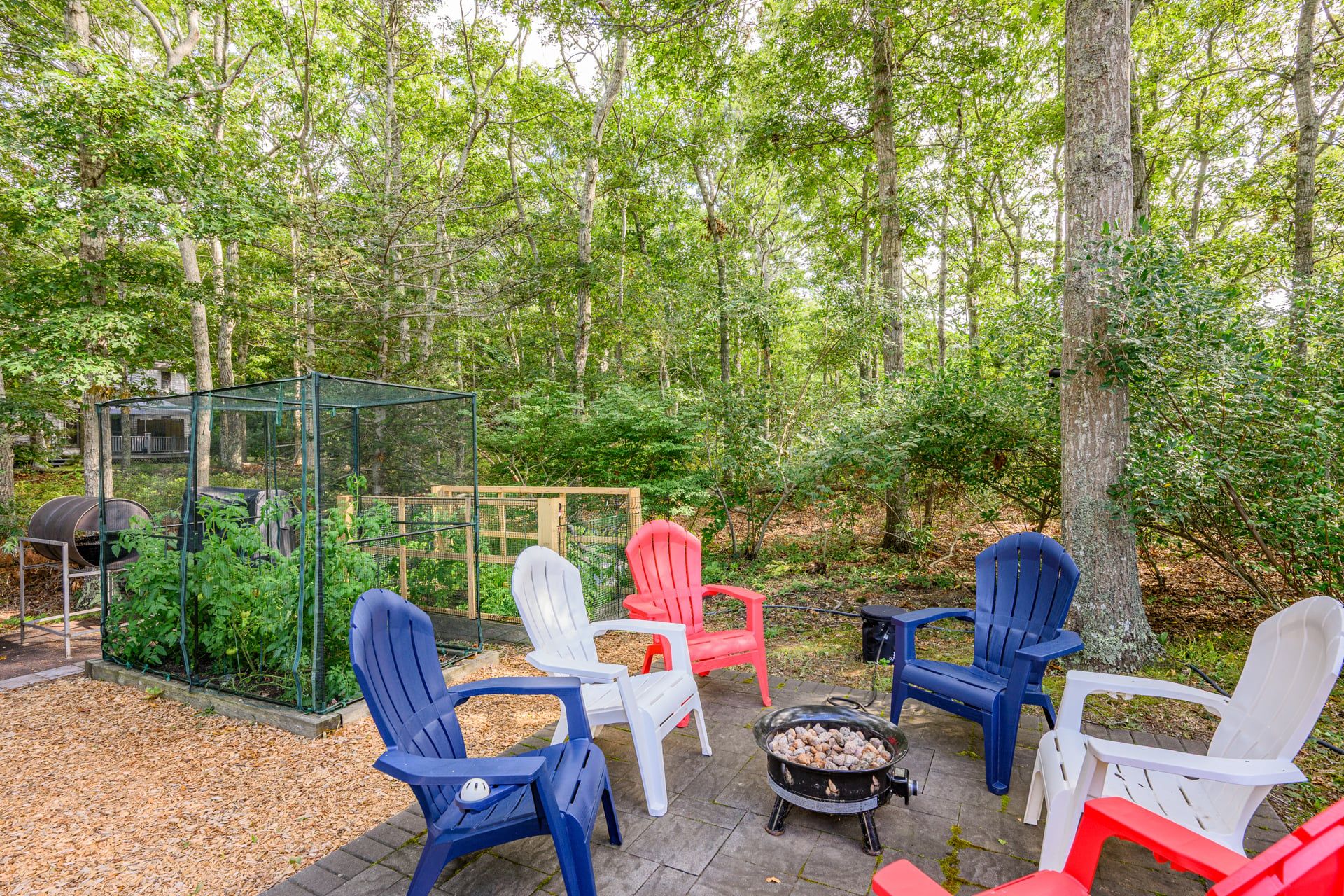 Et udendørs opholdsområde med Adirondack-stole, pejse og et drivhus.