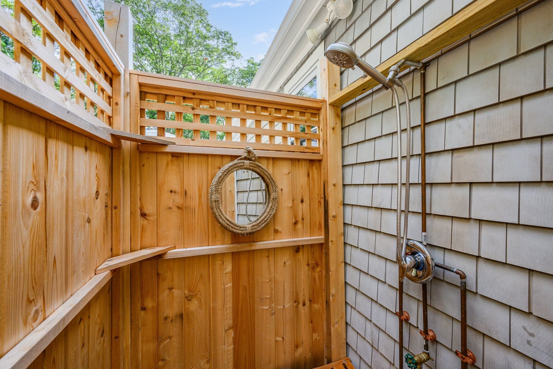 A wooden outdoor shower enclosure with a metal hose and showerhead.