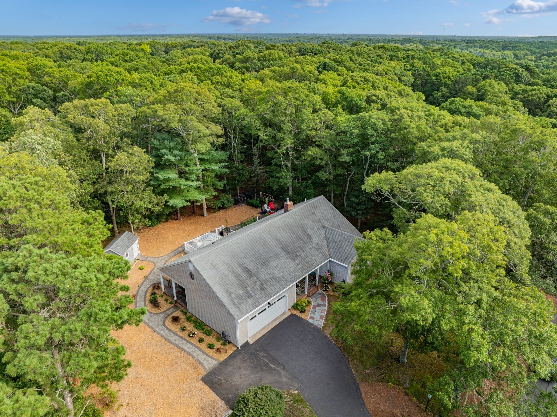 A house surrounded by dense forest with a large garage and a covered porch.