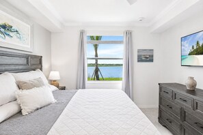 Quarto com cama, mesa de cabeceira, cômoda e janela com vista para um lago e árvores.