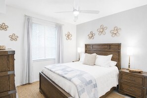Ein Schlafzimmer mit einem hölzernen Bett, weißer Bettwäsche, einem Deckenventilator und blumengeschmückten Wänden.