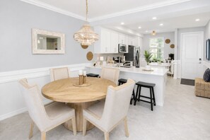 Eine moderne Küche mit weißen Schränken, einer zentralen Kochinsel und einem Essbereich mit rundem Holztisch und Stühlen.