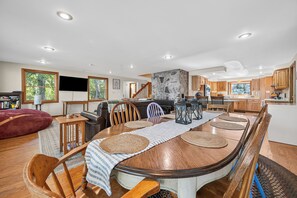A spacious living area with a large wooden dining table, comfortable seating, and a stone accent wall. - Three Loons | Waterfront on Mooselookmeguntic! (Oquossoc)