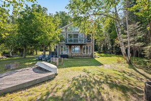 A two-story cabin with a deck, surrounded by trees. - Three Loons | Waterfront on Mooselookmeguntic! (Oquossoc)