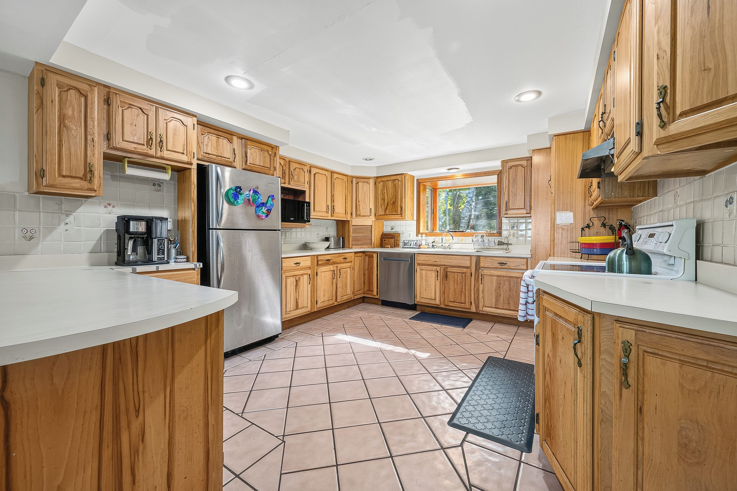 A modern kitchen with wooden cabinets, stainless steel appliances, and a large window.
