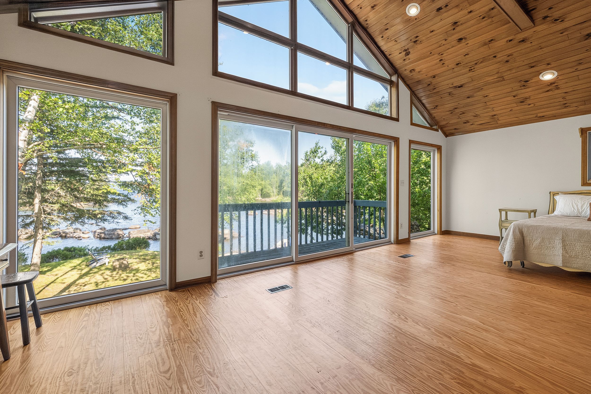A spacious room with large windows, a wooden ceiling, and a bed with a white bedspread.