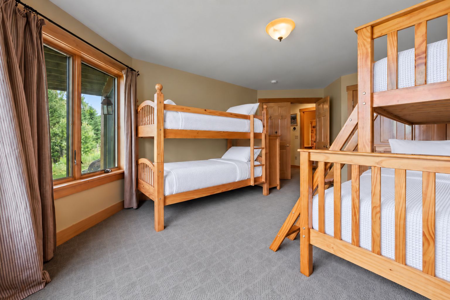 Een kamer met stapelbedden, een trap en uitzicht door een raam.