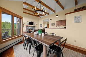 A dining area with a wooden table, chairs, and a fireplace. - Rock Pond Black Gnat 16 | Saddleback Mountain (Sandy River Plantation)