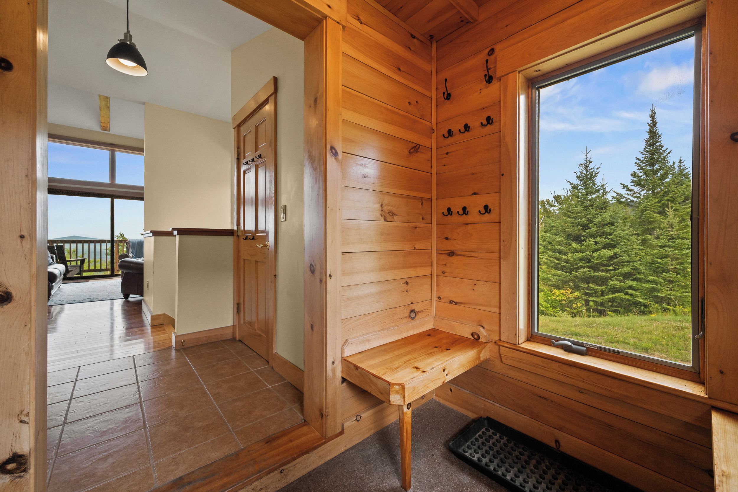 A wooden cabin interior with a bench, a window with a forest view, and a door leading to a balcony.