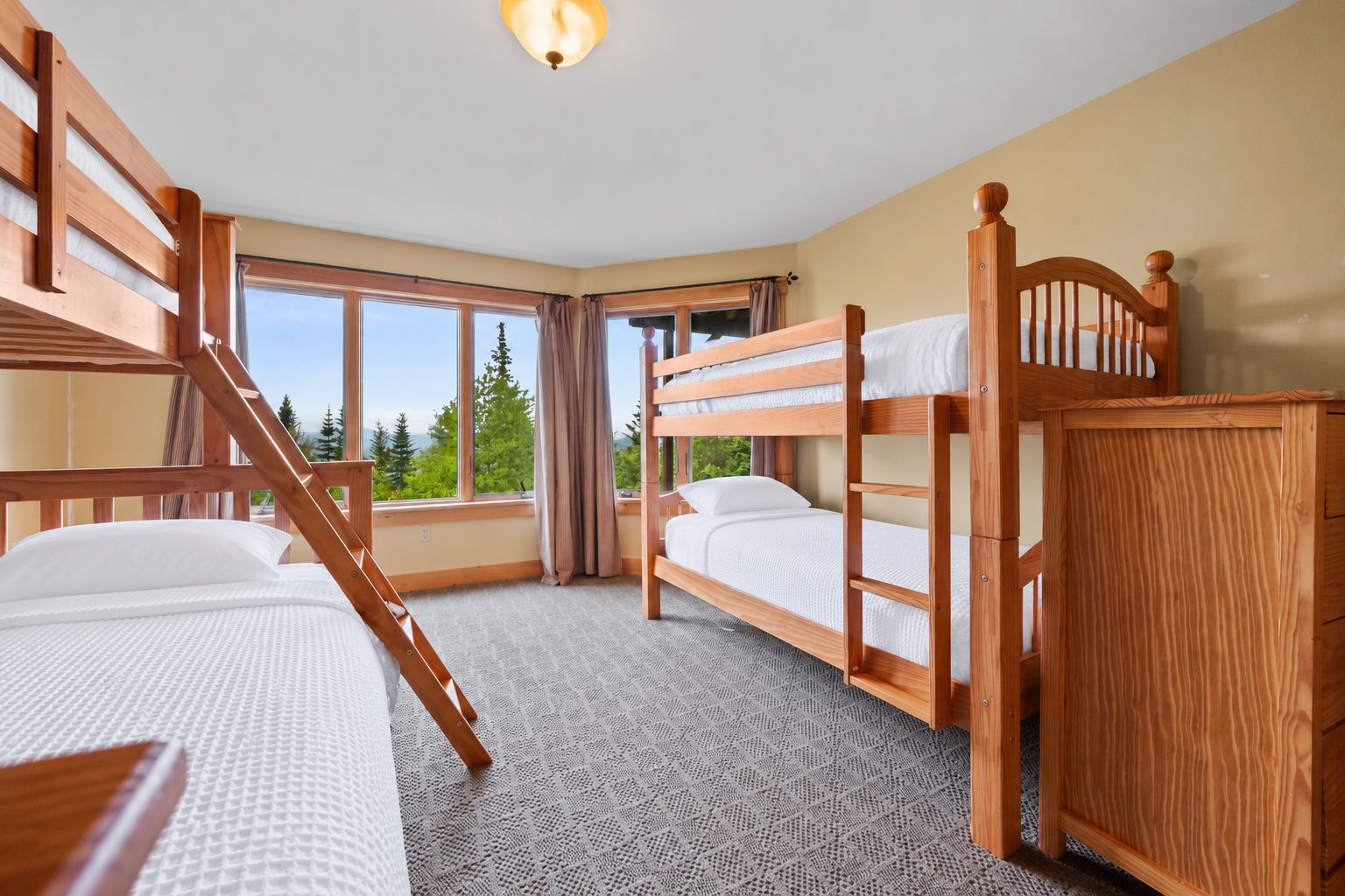 A room with bunk beds, a window with a view of trees, and a carpeted floor.