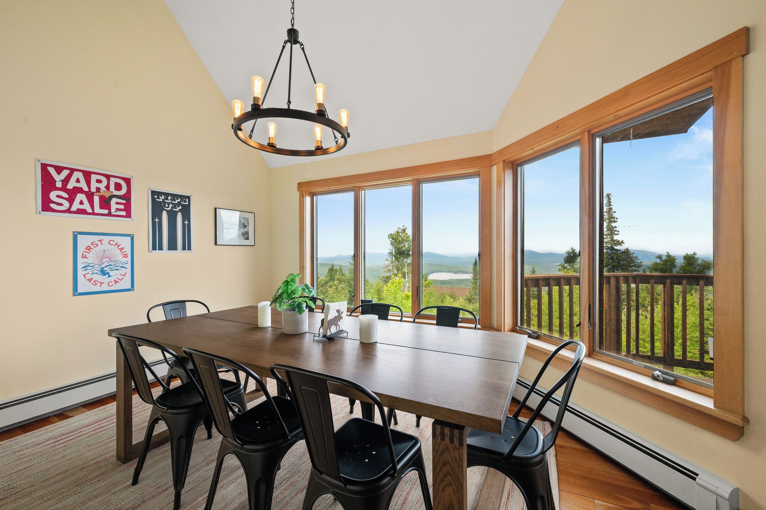 A dining area with a large table, chairs, a chandelier, and a view of a landscape through large windows.