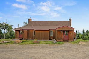A wooden cabin with a red door, chimney, and a gravel driveway. - Rock Pond Black Gnat 16 | Saddleback Mountain (Sandy River Plantation)