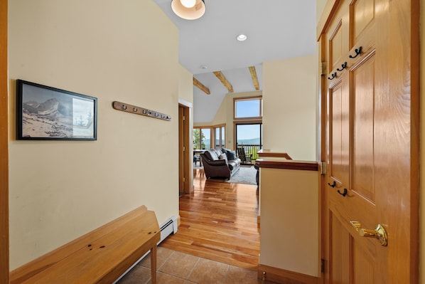 A hallway with wooden benches, a framed picture on the wall, and a door with a coat hook. - Rock Pond Black Gnat 16 | Saddleback Mountain (Sandy River Plantation)