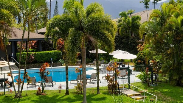 A pool area with lounge chairs and umbrellas, surrounded by palm trees and a mountainous backdrop. - Mauna Kai, Princeville | 3 Bedrooms, AC & Pool (Princeville)