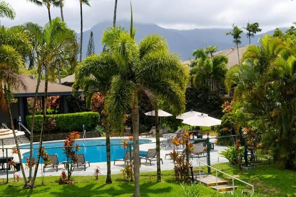 Un espace piscine agrémenté de chaises longues et de parasols, entouré de palmiers et dominé par un paysage montagneux.