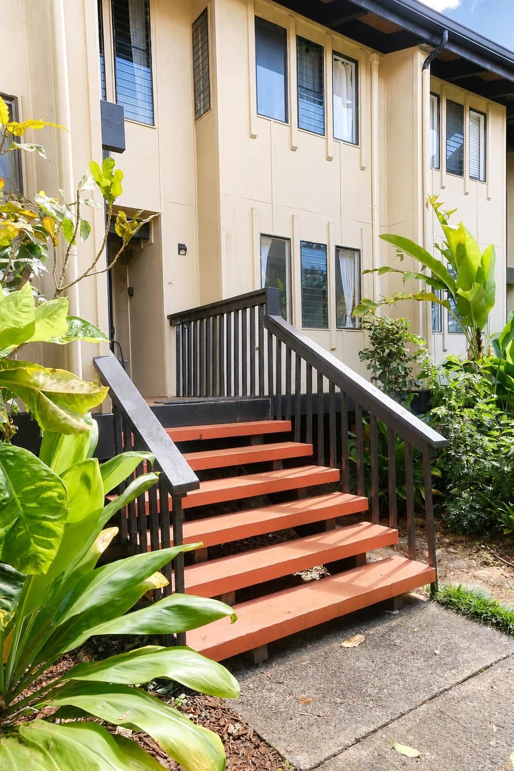 A set of outdoor wooden stairs leading to a building entrance, surrounded by greenery.