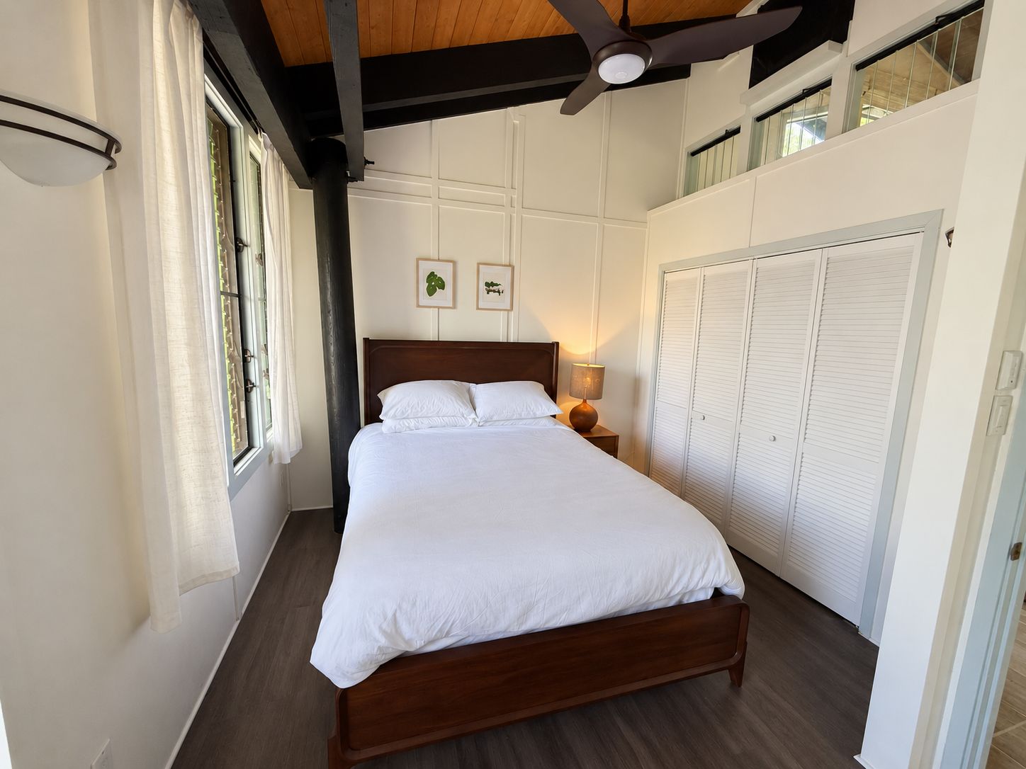 A bedroom with a large bed, a ceiling fan, a window with curtains, and a wardrobe.