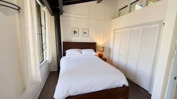 A bedroom with a large bed, a ceiling fan, a window with curtains, and a wardrobe.