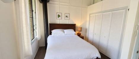 Un dormitorio con una cama grande, un ventilador de techo, una ventana con cortinas y un armario.