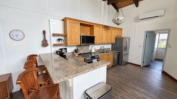 A kitchen with wooden cabinets, a microwave, a refrigerator, and a sink. There is a clock on the wall and a guitar leaning against the wall.