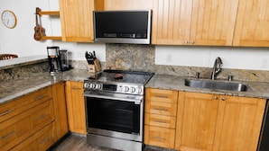 Une cuisine avec des meubles en bois, une cuisinière en acier inoxydable, un four à micro-ondes et un plan de travail en granit.