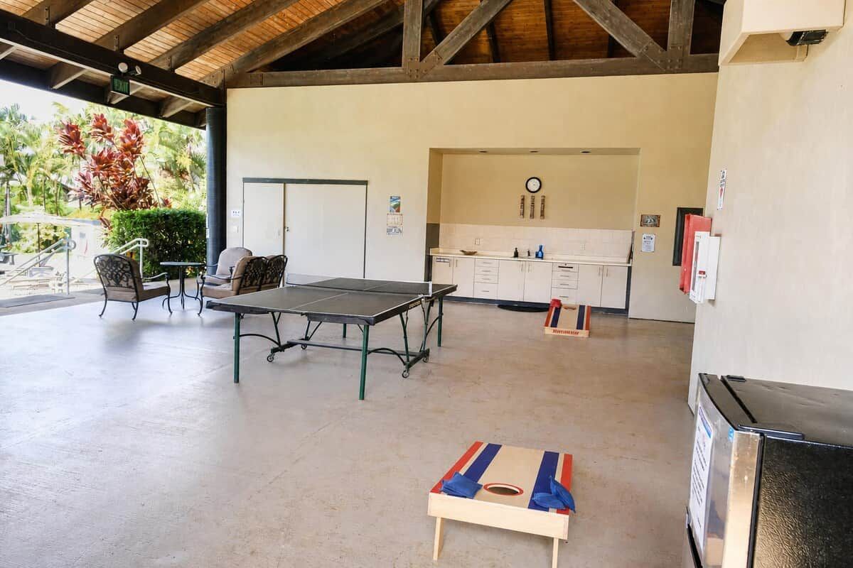 A covered outdoor area with a ping pong table, chairs, a small table, and a refrigerator.