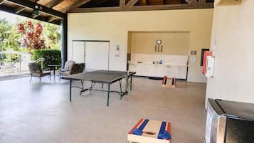 A covered outdoor area with a ping pong table, chairs, a small table, and a refrigerator.