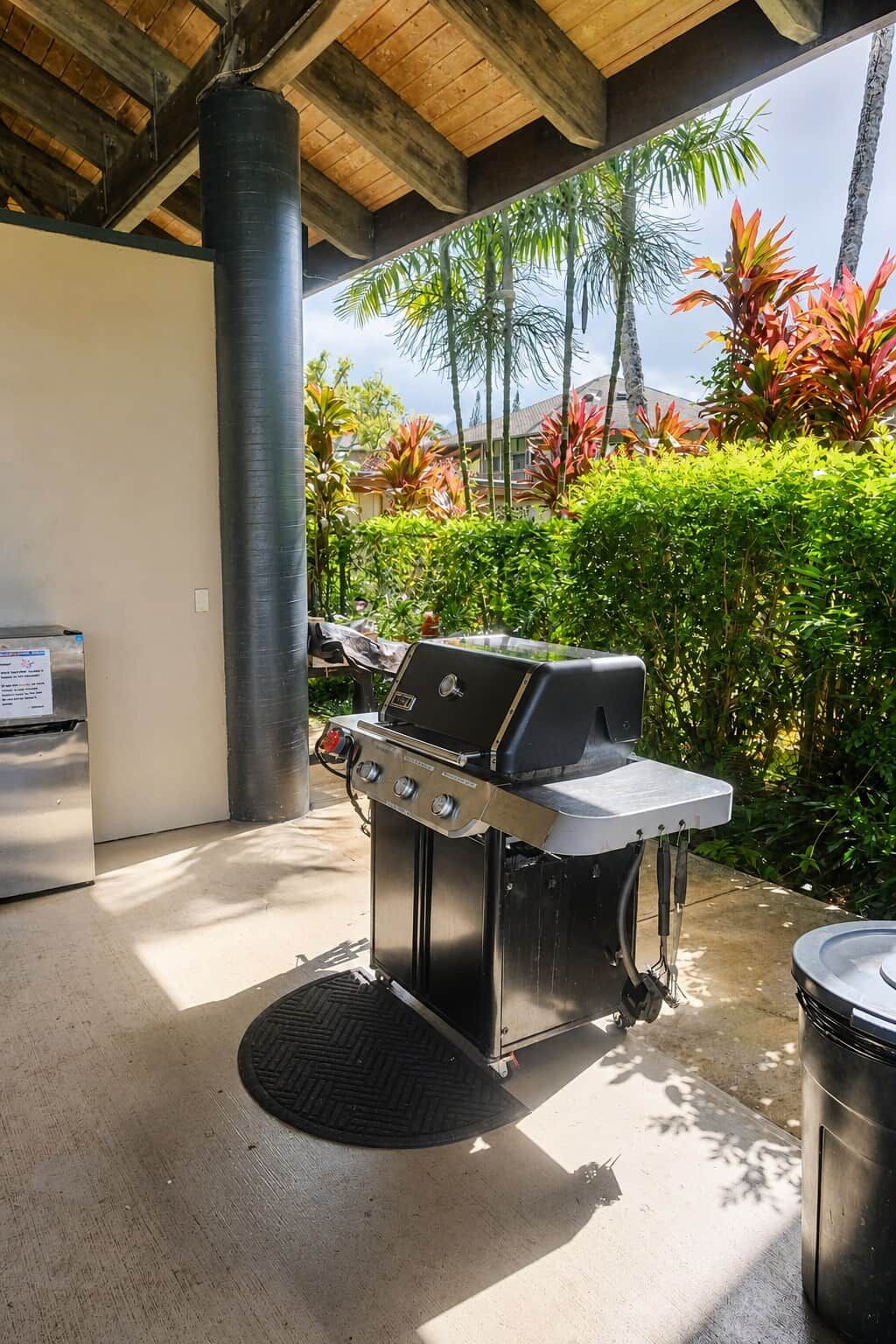 An outdoor grill area with a stainless steel grill, a trash can, and a black mat.
