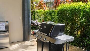 An outdoor grill area with a stainless steel grill, a trash can, and a black mat.