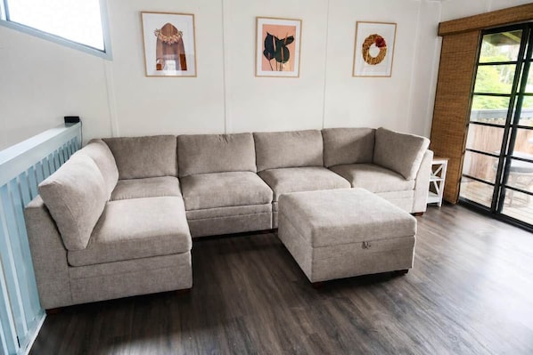 Ein neutral gefärbtes Ecksofa in einem Raum mit einem großen Fenster, einem gerahmten Kunstwerk an der Wand und einer Heizung.